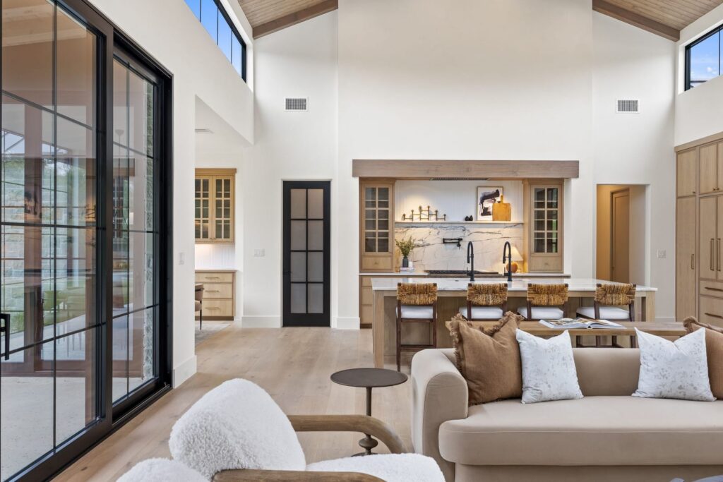 Open living area with a marble kitchen island, four woven bar stools, and large windows letting in natural light.