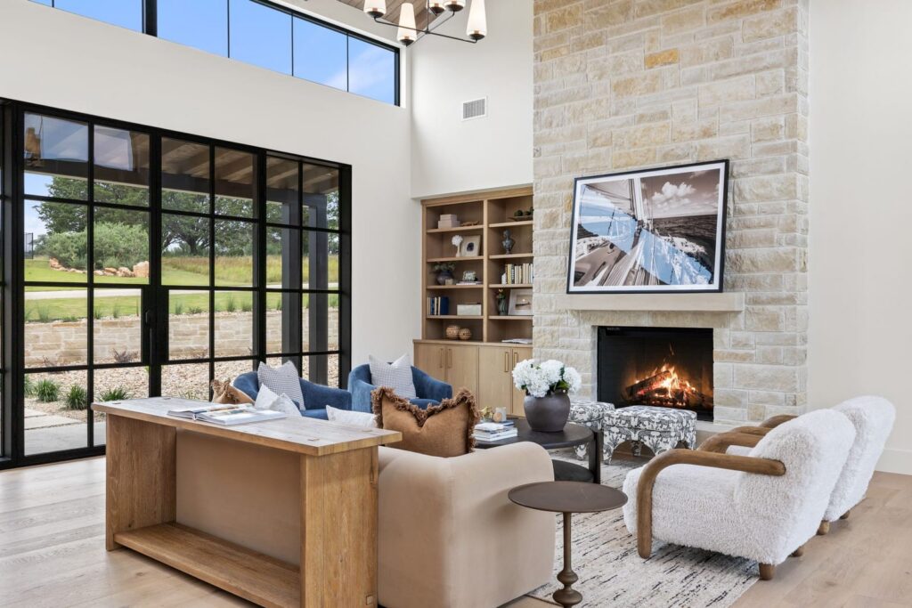 Bright, modern living room with large black-framed glass doors, a stone fireplace, and plush seating facing the fireplace.