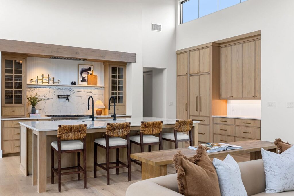 Bright modern kitchen with a large marble-topped island, four wooden-bar stools, and light wood cabinetry.",